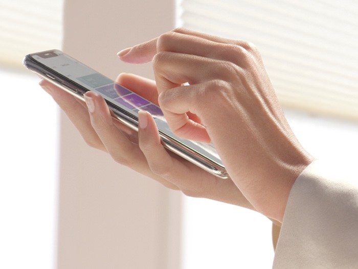 Une personne utilisant un téléphone intelligent pour contrôler les parures de fenêtre à partir d’une application grâce à l’automatisation PowerViewMD.
