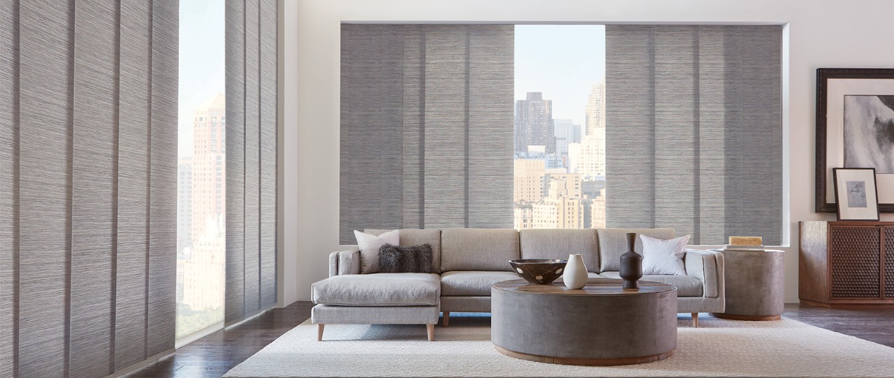 Un grand salon avec de grandes fenêtres équipées de panneaux de fenêtre coulissants Skyline®; tissu : Maya; couleur : gris Zanzibar